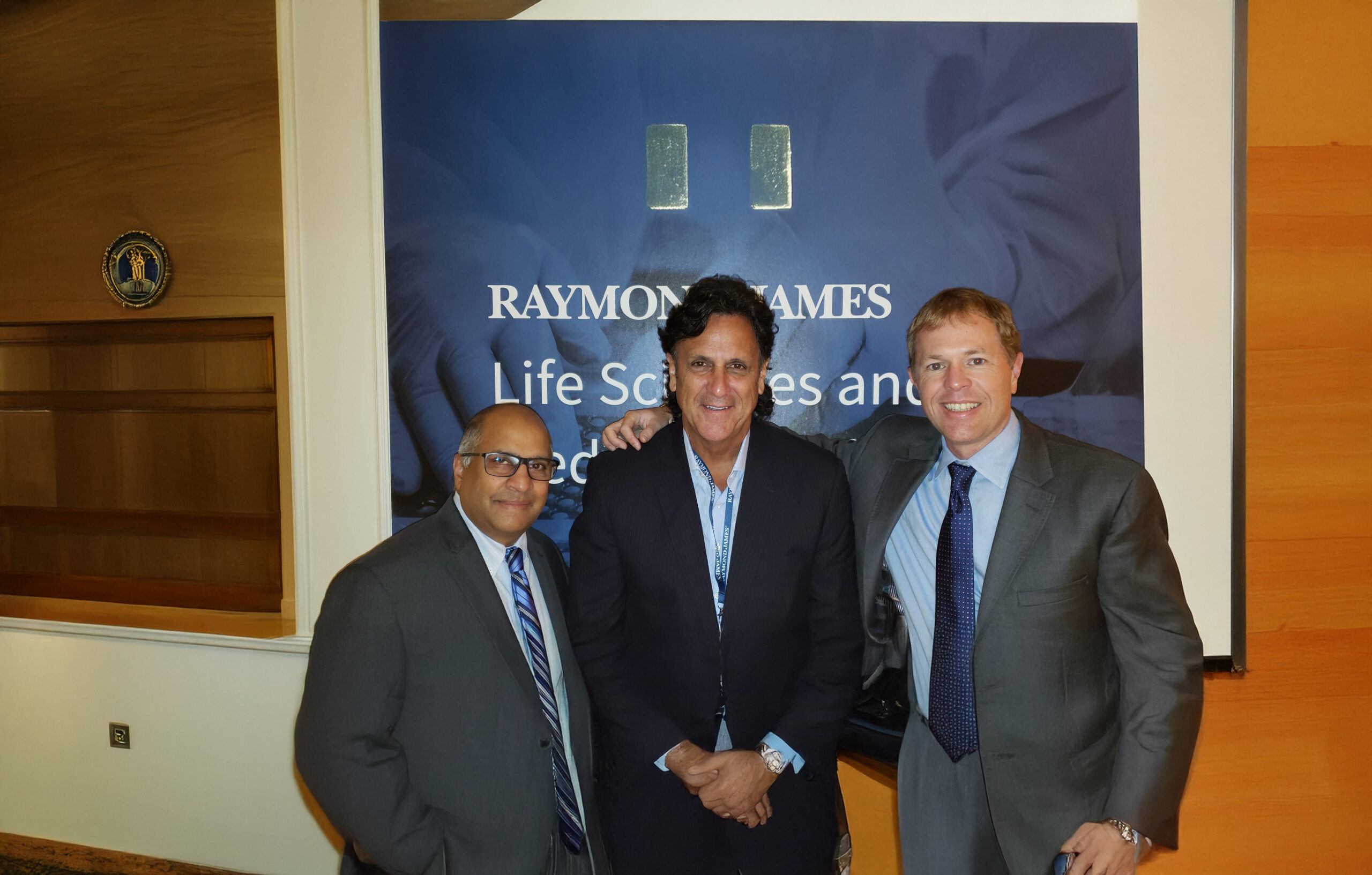 Three men in formal suits and ties stand together, smiling for a posed photograph.